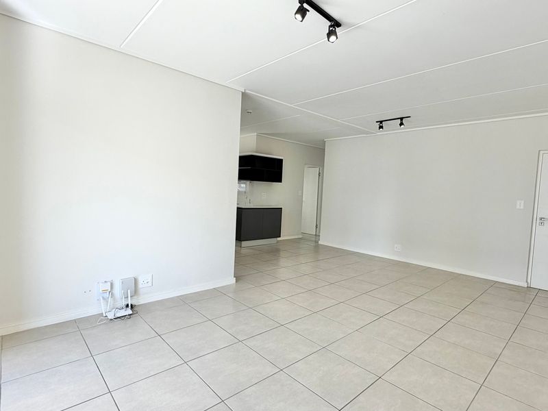 Spacious open-plan living area featuring neutral tiled flooring, modern track lighting, and a glimpse into the adjacent kitchen space.