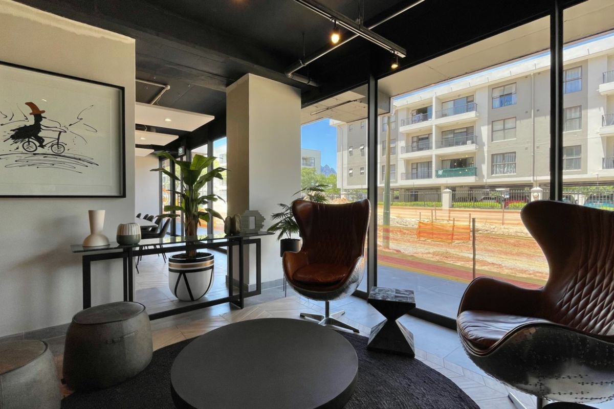 Modern living area featuring floor-to-ceiling windows, exposed black ceilings with track lighting, and stylish herringbone tile flooring with views of the surrounding complex.