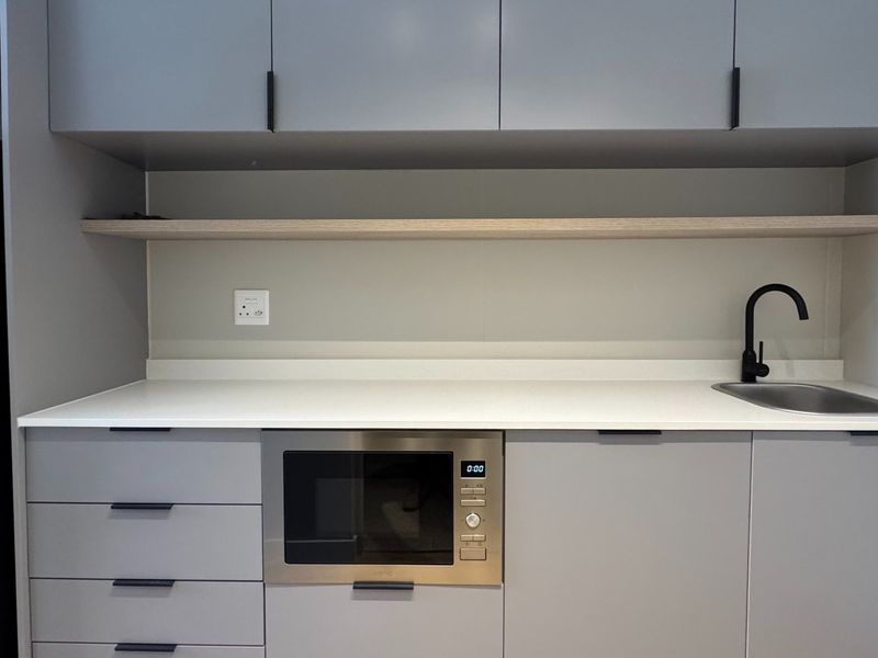 Modern kitchen featuring sleek grey cabinetry, white quartz countertops, an undermount sink with a black mixer tap, and a built-in microwave.