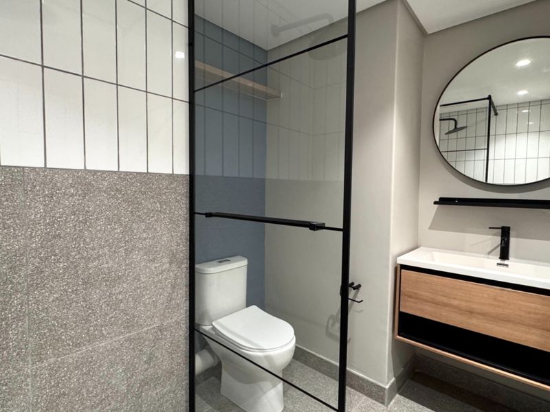 Modern bathroom featuring a floating vanity, black-framed glass shower screen, contemporary subway and terrazzo-style tiling, and a sleek circular mirror.