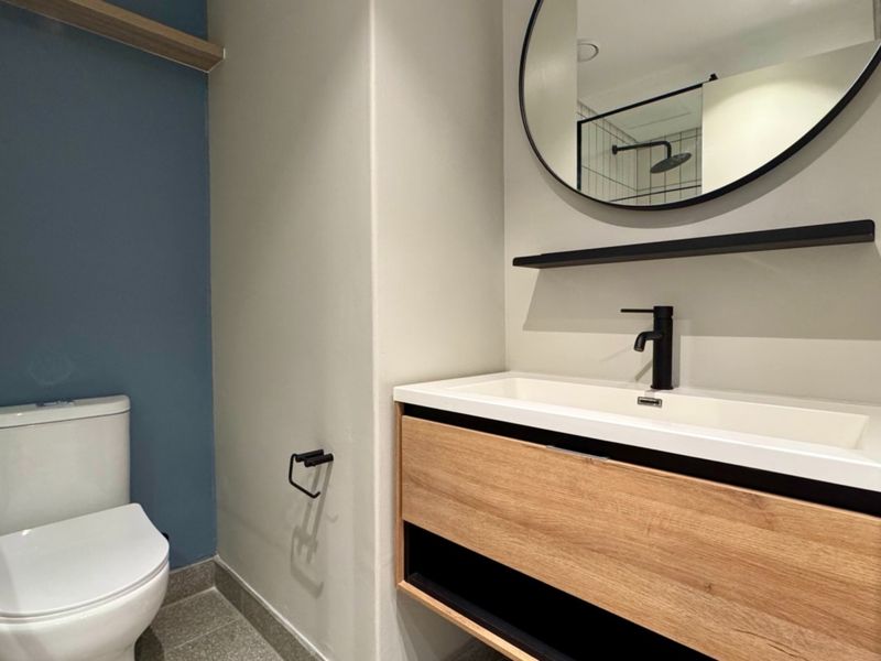 Modern bathroom featuring a wall-mounted timber-look vanity with integrated basin, black fixtures, and a sleek walk-in shower enclosure.