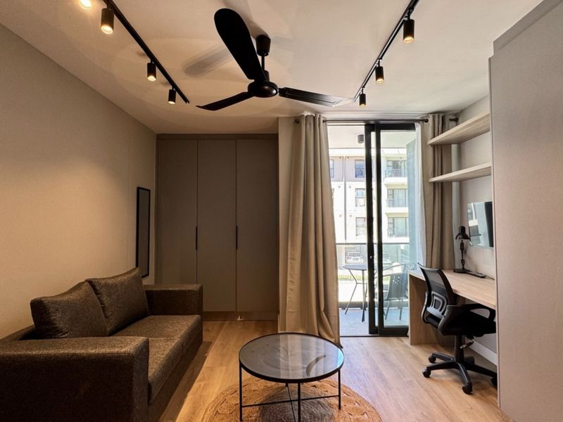 Modern bedroom featuring built-in cupboards, a dedicated workspace with floating shelves, track lighting, and direct access to a private balcony.