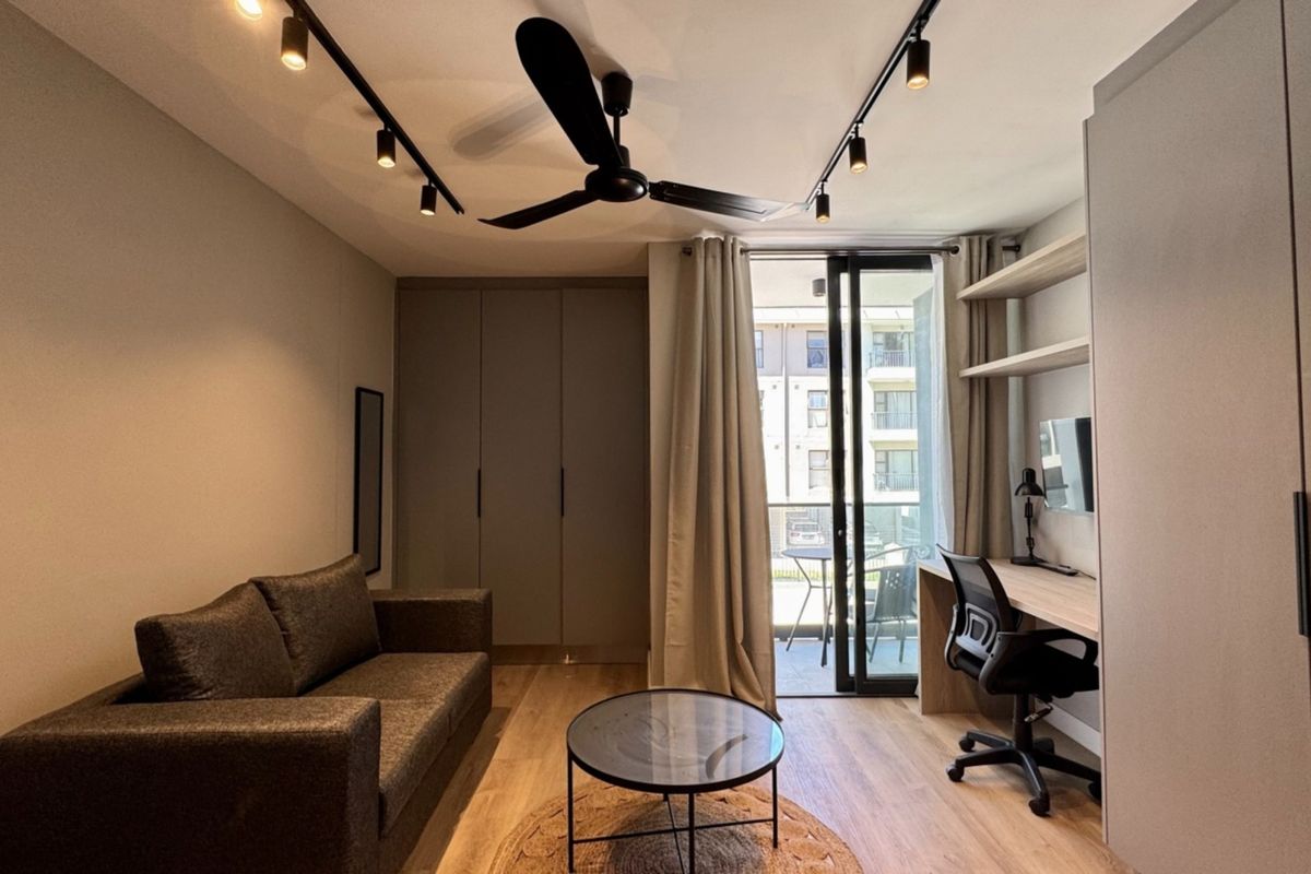 Modern bedroom featuring built-in cupboards, a dedicated workspace with floating shelves, track lighting, and direct access to a private balcony.