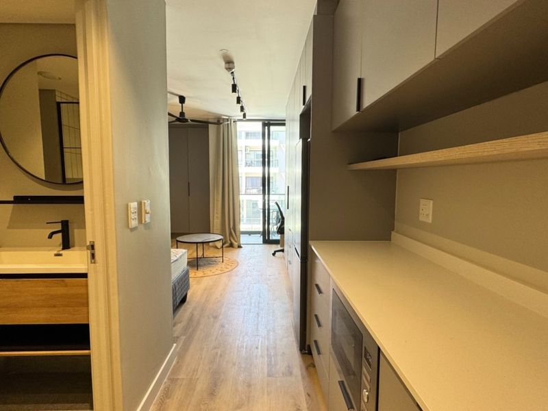Modern open-plan apartment featuring a sleek kitchen with stone countertops, integrated appliances, and an adjacent bathroom with a contemporary vanity.