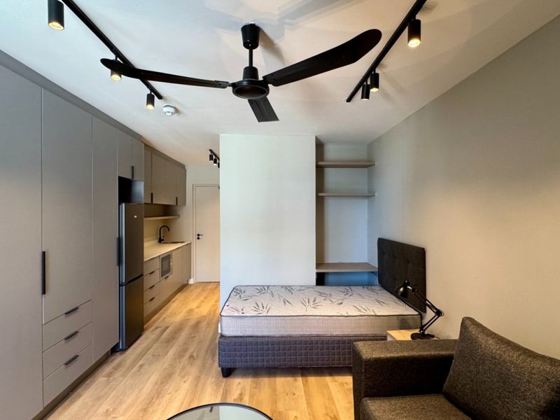 Modern open-plan studio apartment featuring sleek built-in cabinetry, integrated kitchen facilities, contemporary track lighting, and durable laminate flooring throughout.