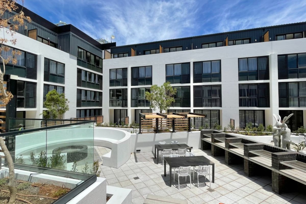 A well-maintained communal outdoor terrace featuring built-in brick barbecue stations, paved flooring, and glass balustrades, set against a modern multi-story apartment building.