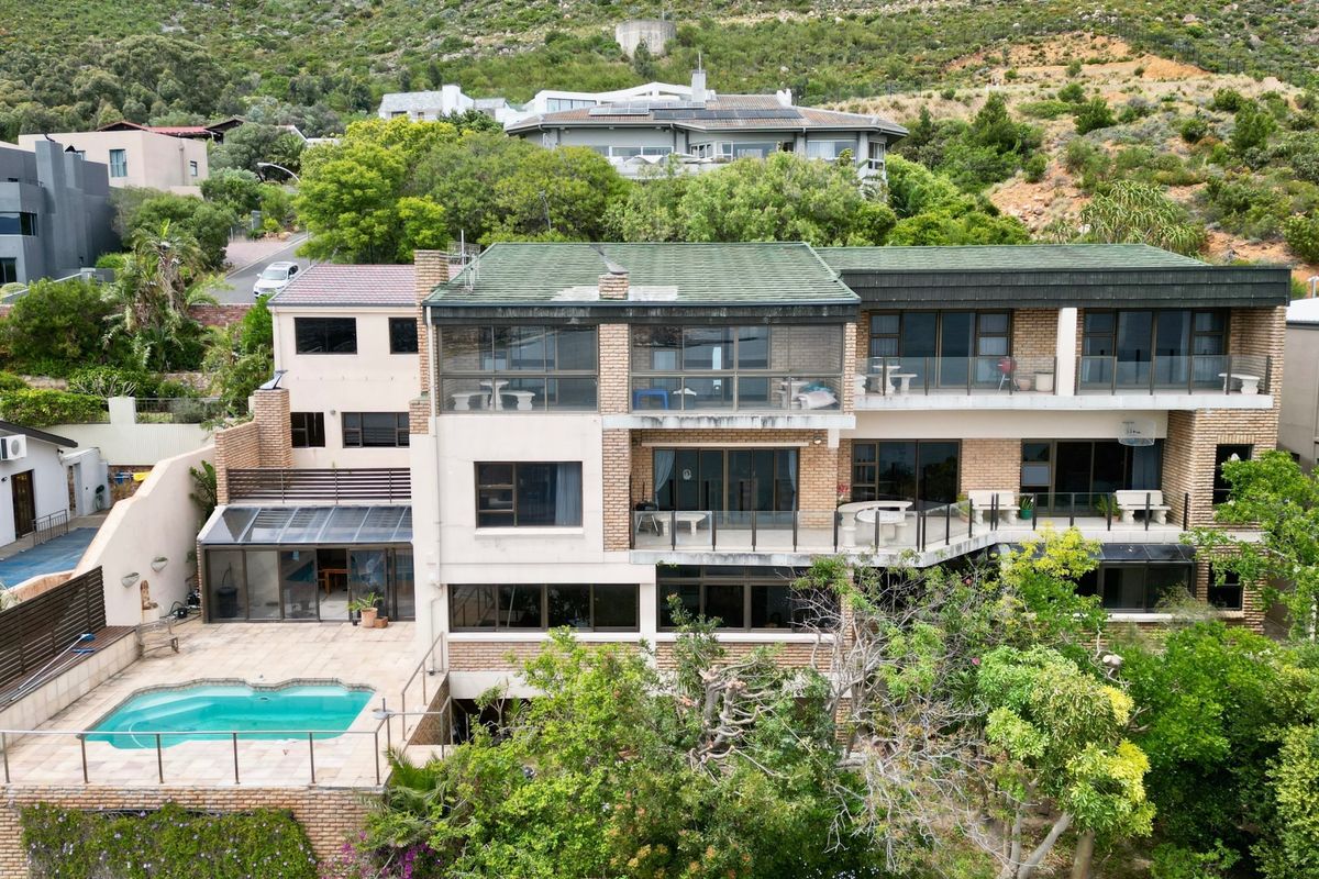 Aerial view of a multi-story apartment building featuring multiple balconies, a swimming pool, and established garden surroundings set against a hillside.