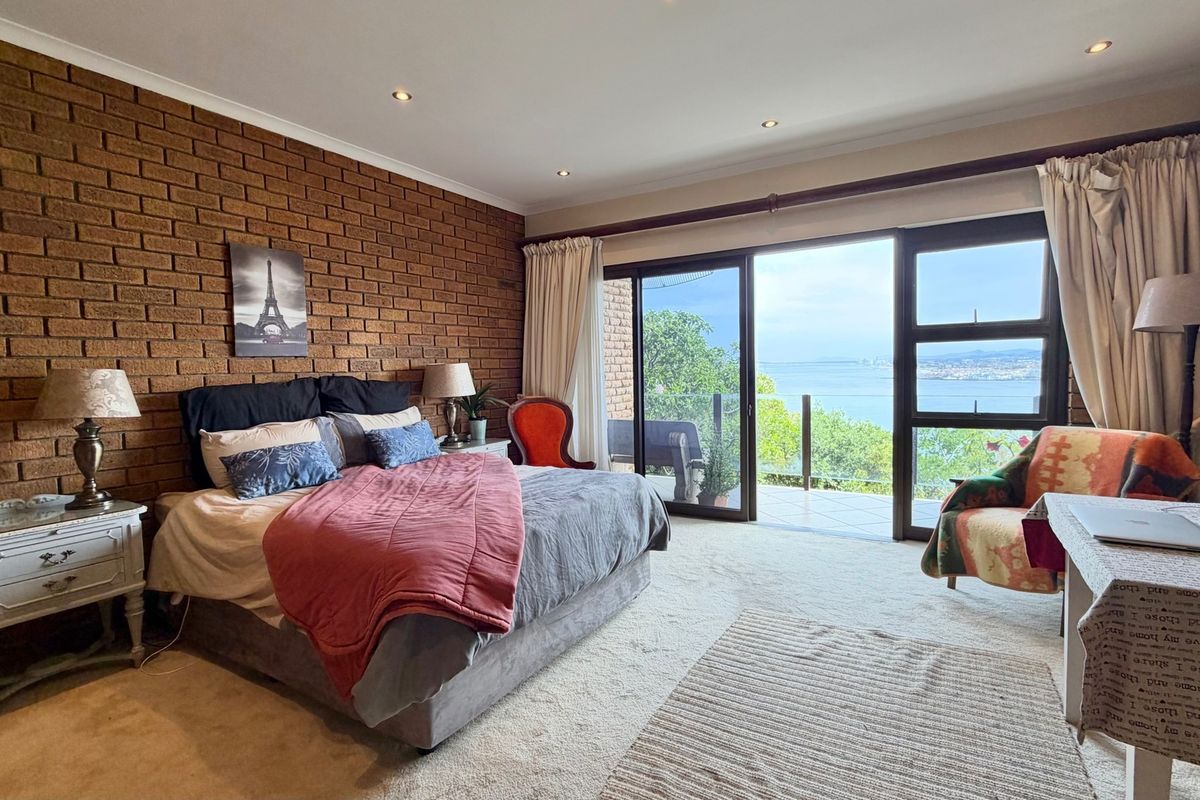 Spacious bedroom featuring an exposed brick feature wall, recessed lighting, and large sliding glass doors opening onto a balcony with scenic water views.
