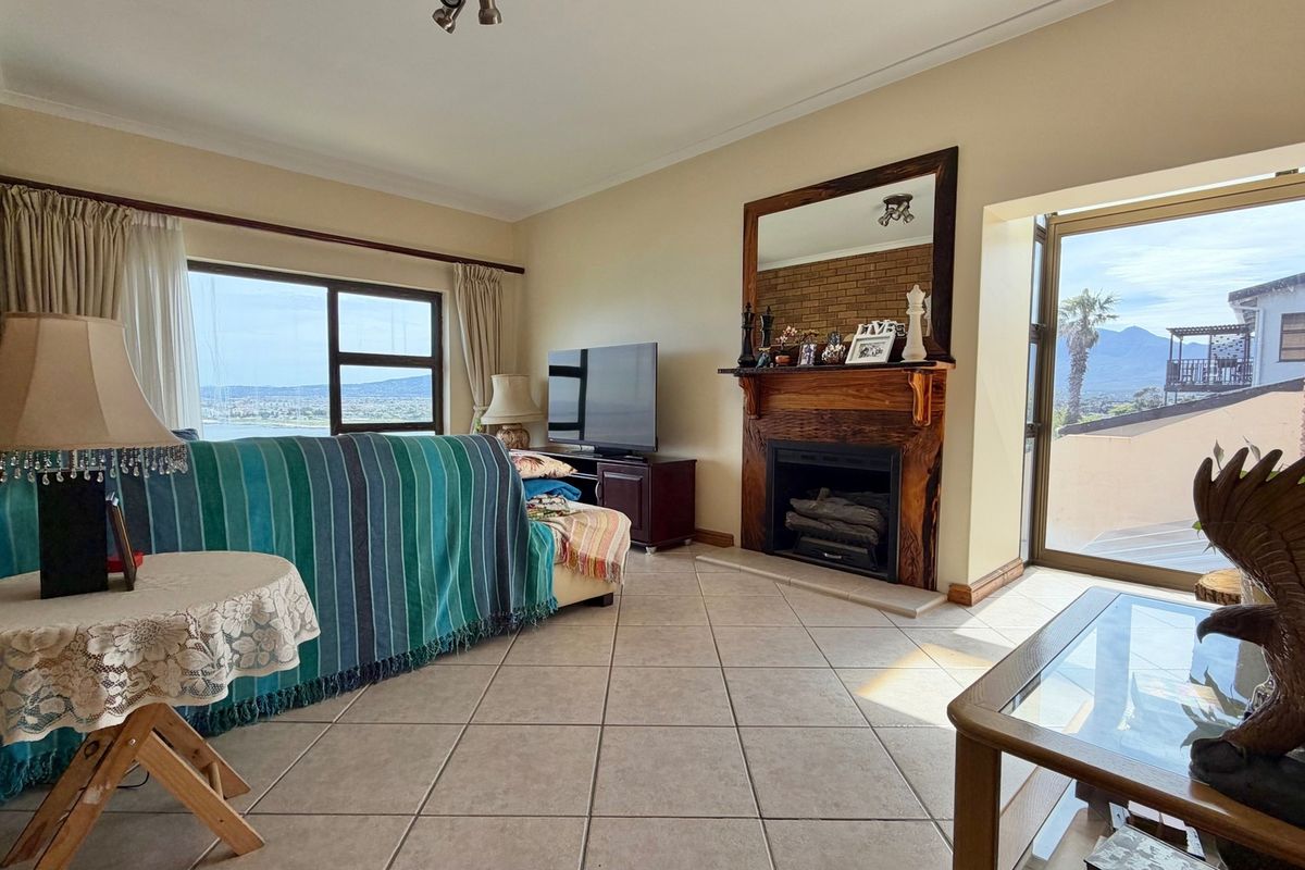 Spacious living room featuring a brick accent wall, a traditional fireplace with a wooden mantel, tiled flooring, and large windows with scenic views.