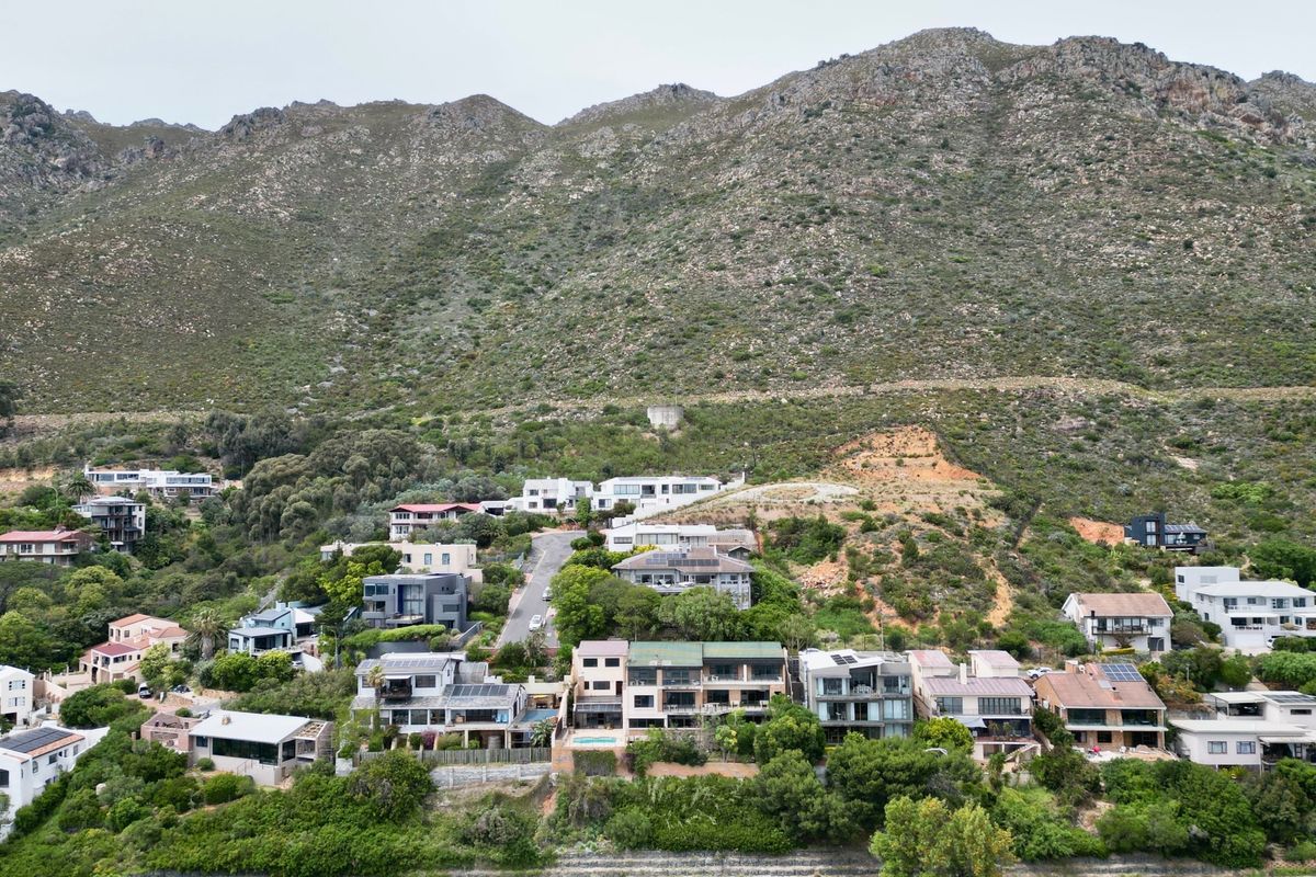 An aerial view of a residential hillside neighborhood nestled against a large mountain range, showcasing the property's location and surrounding landscape.