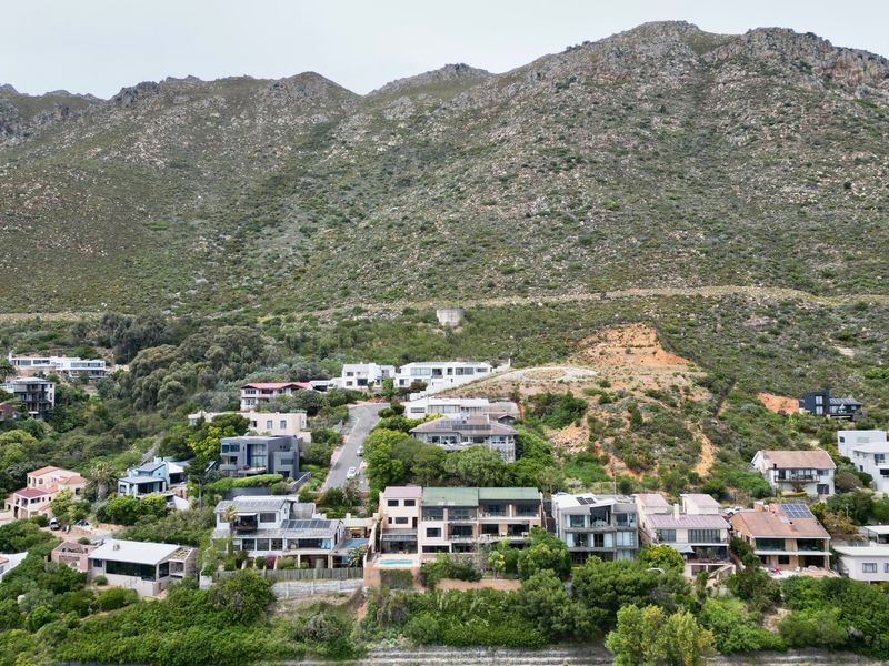 An aerial view of a residential hillside neighborhood nestled against a large mountain range, showcasing the property's location and surrounding landscape.