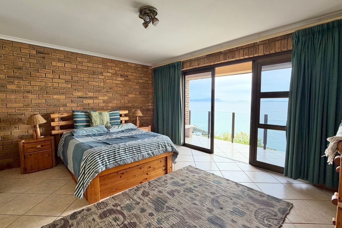 Spacious bedroom featuring an exposed brick feature wall, tiled flooring, and large sliding glass doors opening onto a balcony with scenic ocean views.