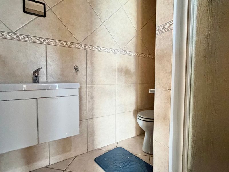 A functional bathroom featuring a wall-mounted vanity with a ceramic basin, toilet, and neutral ceramic wall and floor tiling with a decorative border.
