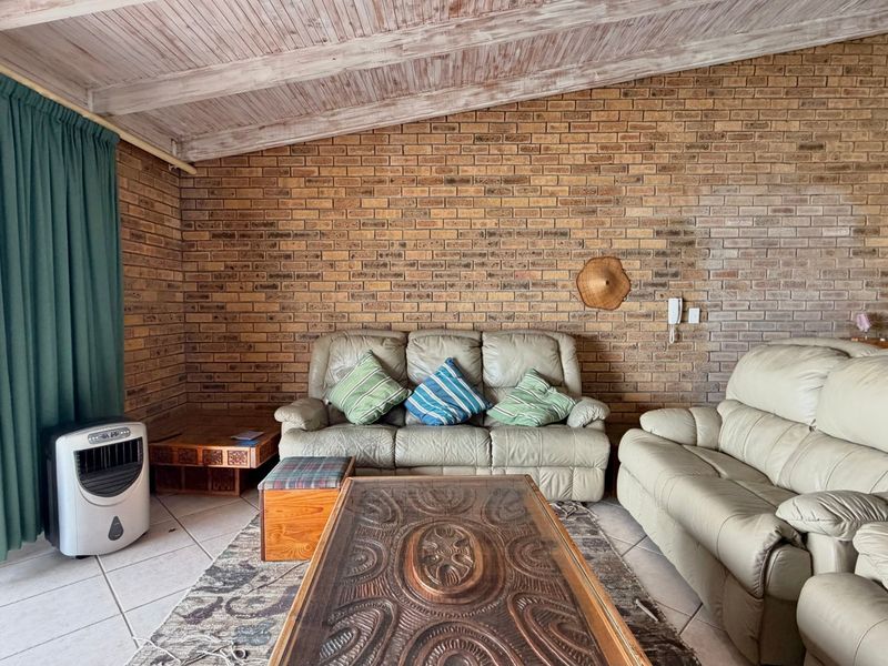 Living room featuring a rustic facebrick wall, exposed timber ceiling beams, and tiled flooring with direct access to an outdoor area via sliding doors.