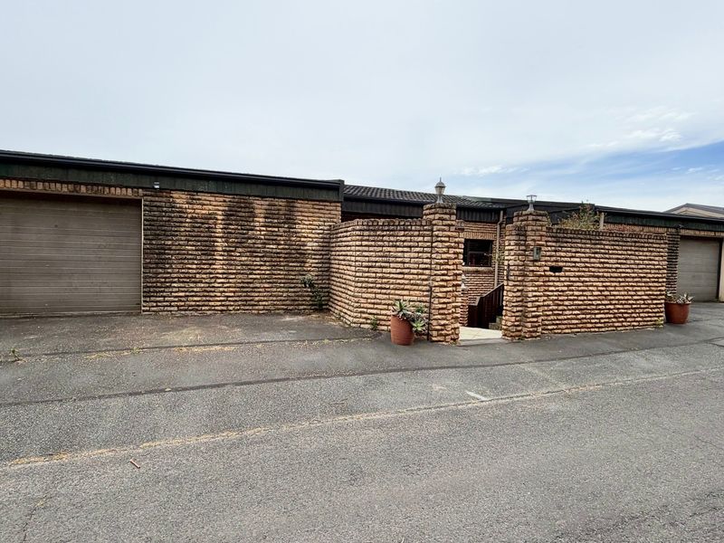 Front exterior view of the property featuring a brick facade, garage access, and a gated entrance, showing signs of weathering and maintenance requirements.