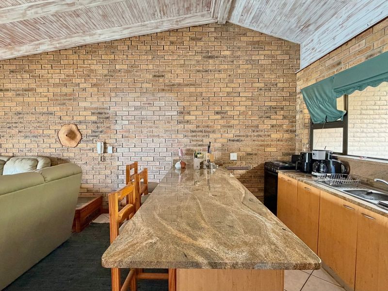 Open-plan living and kitchen area featuring a prominent exposed brick wall, vaulted timber ceiling, and a large granite breakfast bar.