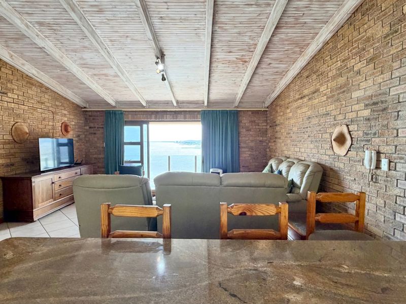 Open-plan living area featuring exposed brick walls, a vaulted timber beam ceiling, and a granite breakfast bar with direct access to a balcony view.