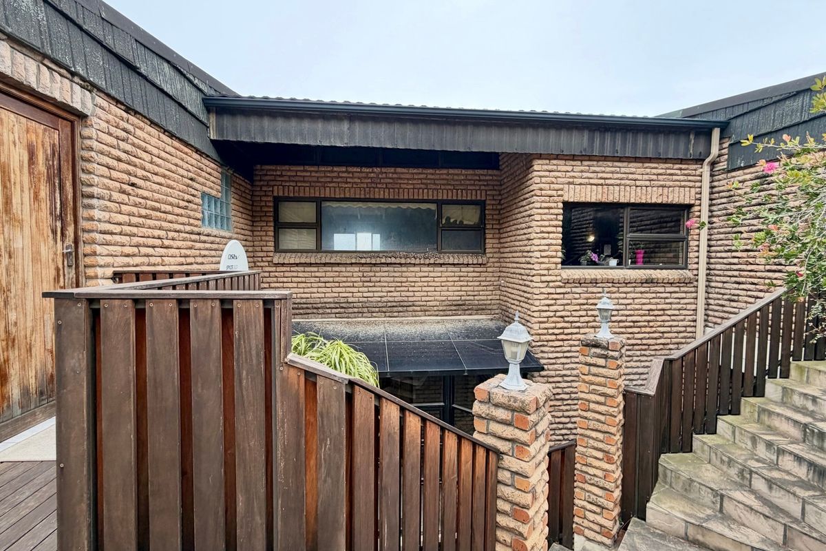 Rear exterior view of the property featuring face brick walls, timber decking, and a staircase with brick pillars and wooden balustrades.