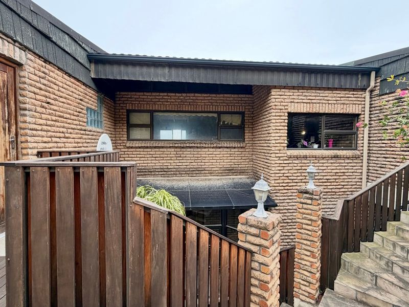 Rear exterior view of the property featuring face brick walls, timber decking, and a staircase with brick pillars and wooden balustrades.