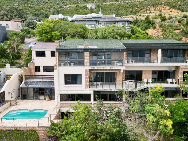 Aerial view of a multi-story apartment building featuring multiple balconies, a swimming pool, and established garden surroundings set against a hillside.