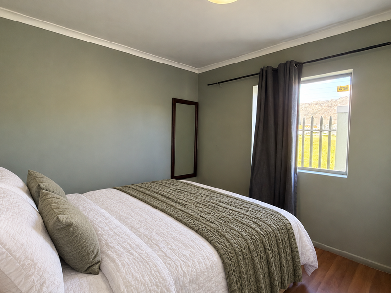 A well-maintained bedroom featuring neutral sage green walls, laminate flooring, and a built-in wardrobe with a view of the surrounding landscape.