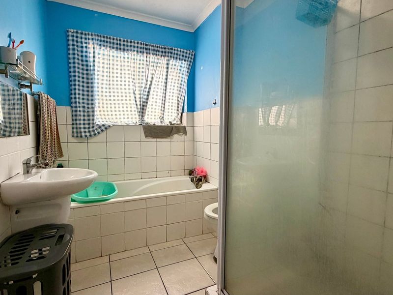 A functional bathroom featuring a bathtub, separate shower enclosure, pedestal basin, and toilet, finished with tiled walls and flooring.