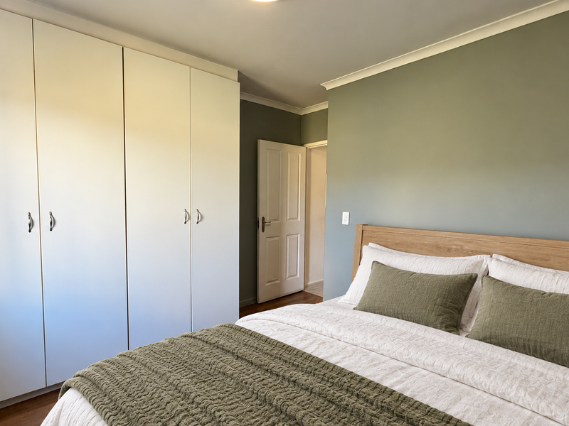 A well-maintained bedroom featuring built-in cupboards, timber flooring, and a neutral color palette with a coved ceiling.