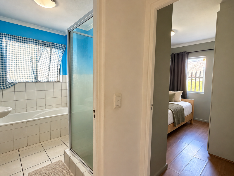 A functional bathroom featuring a pedestal basin, built-in bathtub, and separate shower enclosure, adjacent to a bedroom with laminate flooring.