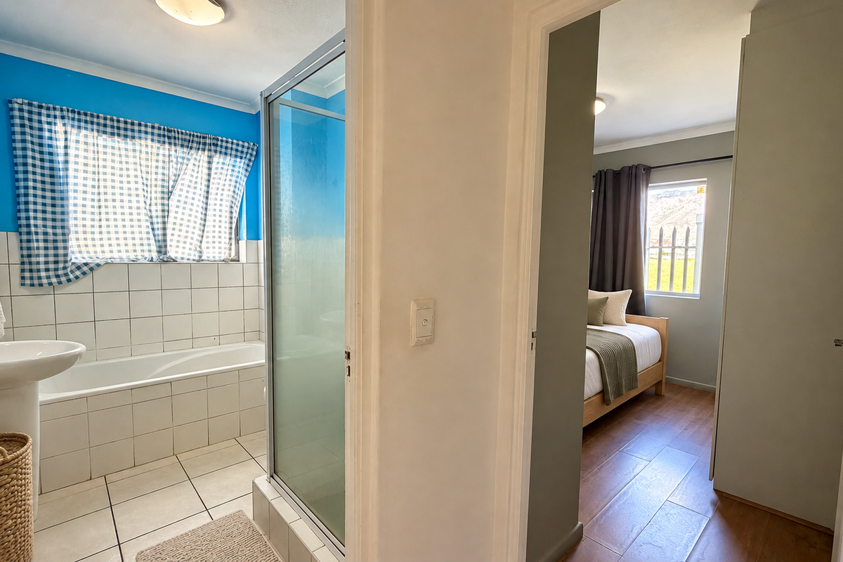 A functional bathroom featuring a pedestal basin, built-in bathtub, and separate shower enclosure, adjacent to a bedroom with laminate flooring.