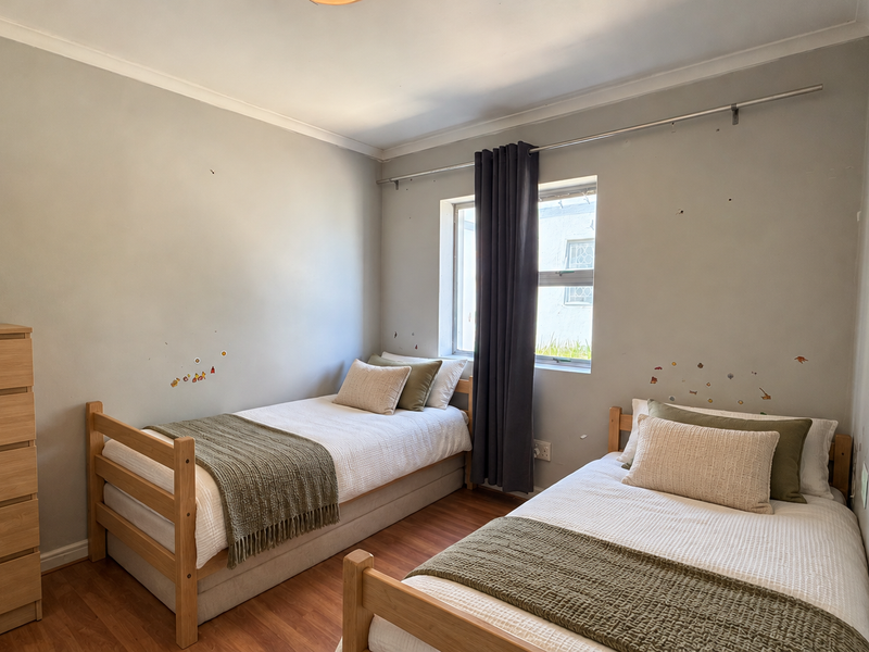 A bedroom featuring laminate flooring and a window with a curtain rod, currently configured with two single beds.