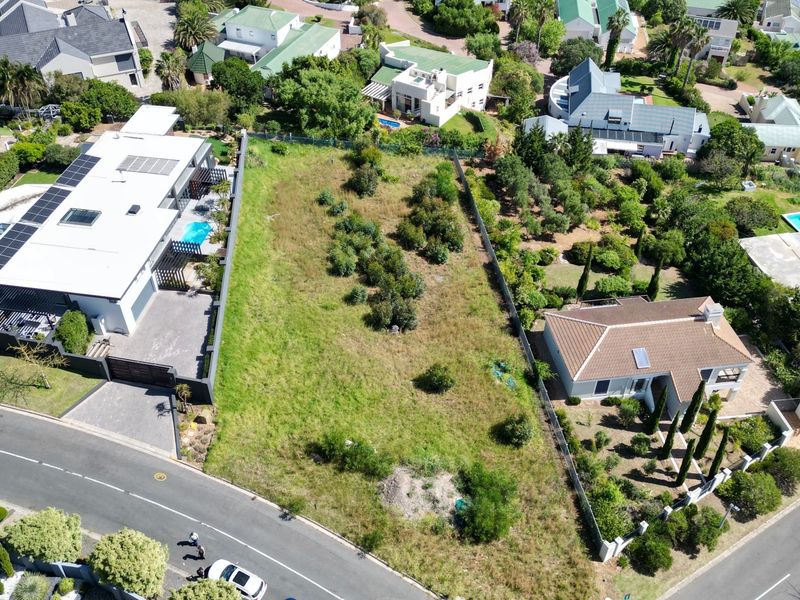 Aerial view of a vacant residential plot situated between established homes, featuring street access and boundary fencing in a developed suburban neighborhood.