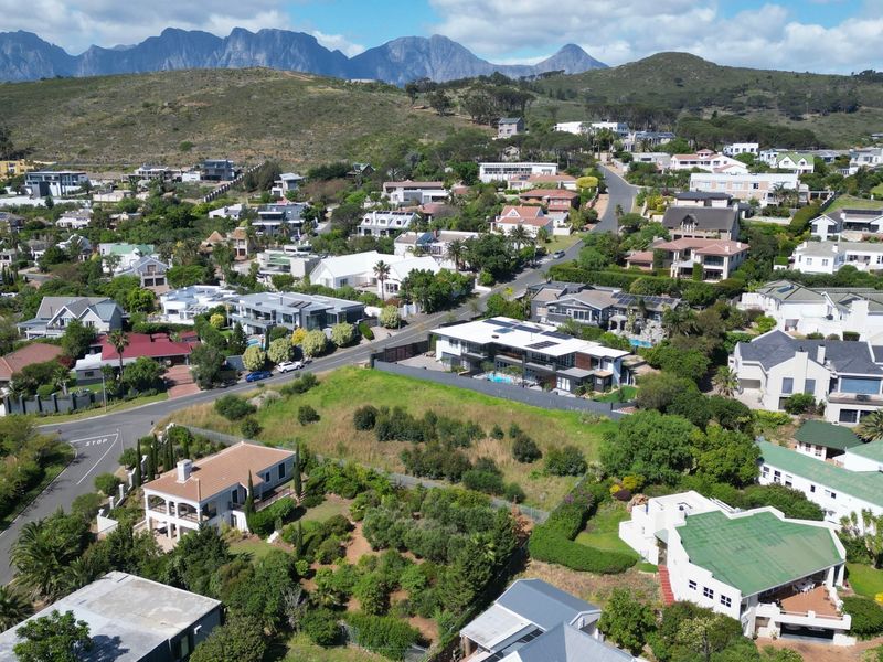 An elevated aerial view of a residential neighborhood featuring established homes, lush greenery, and a scenic mountain range in the background.