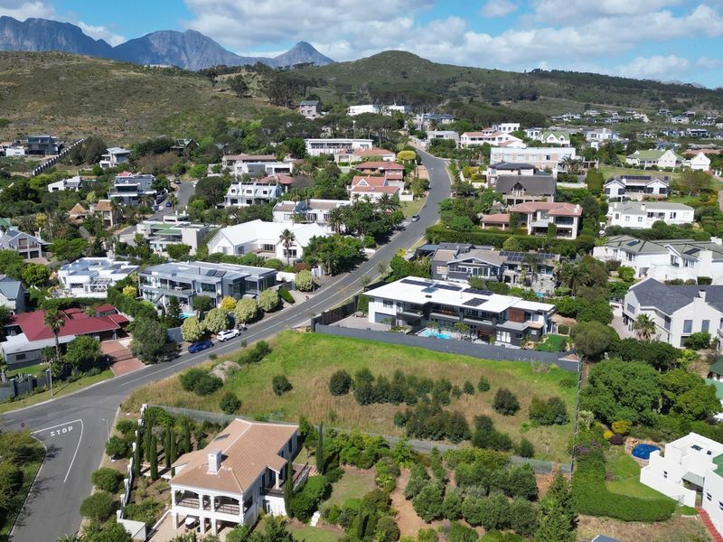 Aerial view of a vacant residential plot situated within an established suburban neighborhood, featuring mountain views and proximity to local road infrastructure.