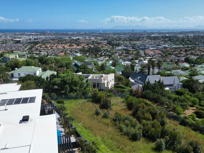 An elevated aerial view showcasing the residential property, surrounding neighborhood, and distant coastal landscape.