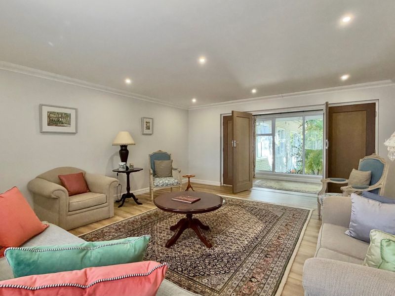A bright and spacious living room featuring recessed downlighting, laminate flooring, and direct access to an outdoor area through double doors.