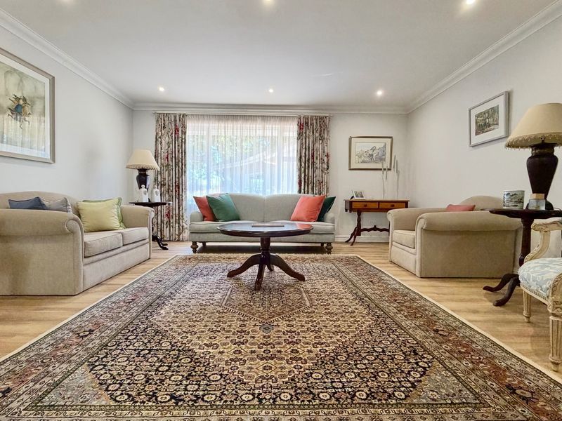 A well-maintained living room featuring recessed downlights, decorative cove cornicing, and light-toned laminate flooring, creating a bright and inviting atmosphere.