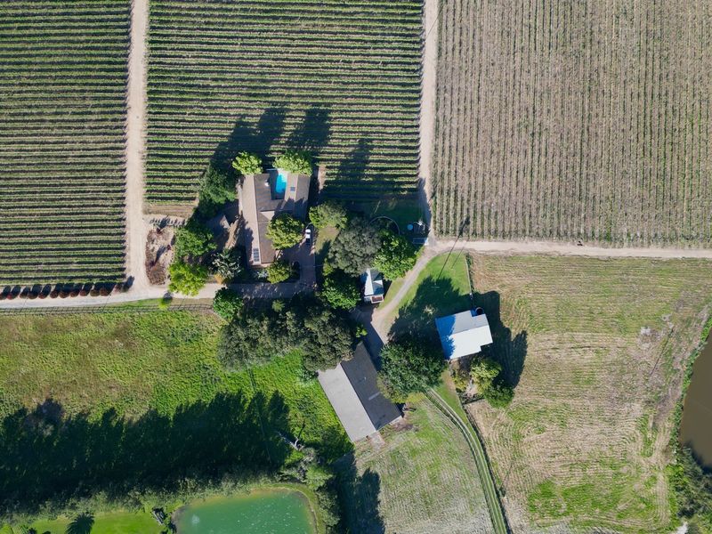Aerial view of a farm property featuring a main residence with a swimming pool, surrounding vineyards, outbuildings, and two farm dams.