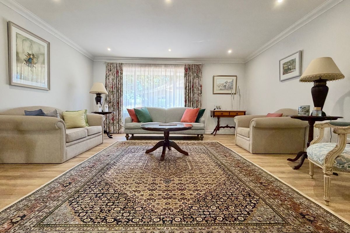 A well-maintained living room featuring recessed downlighting, decorative cove cornicing, and light timber laminate flooring.