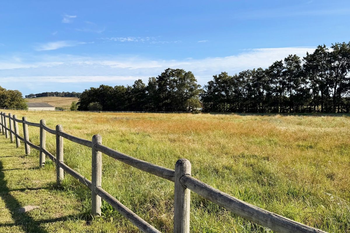 Expansive open pasture land on a farm, enclosed by traditional post and rail timber fencing with decorative lighting.