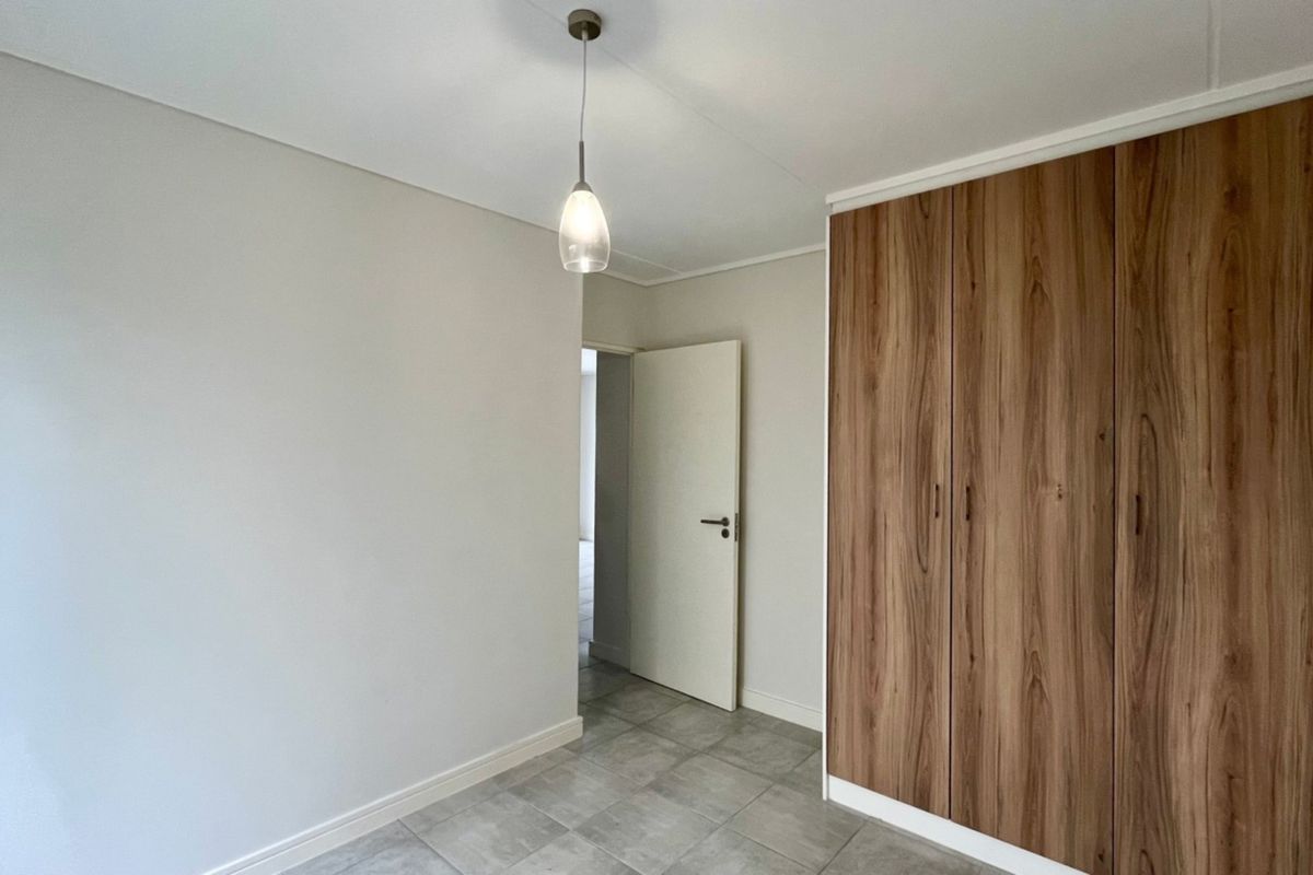 A clean, empty bedroom featuring modern tiled flooring, a built-in wooden wardrobe, and a simple pendant light fixture.
