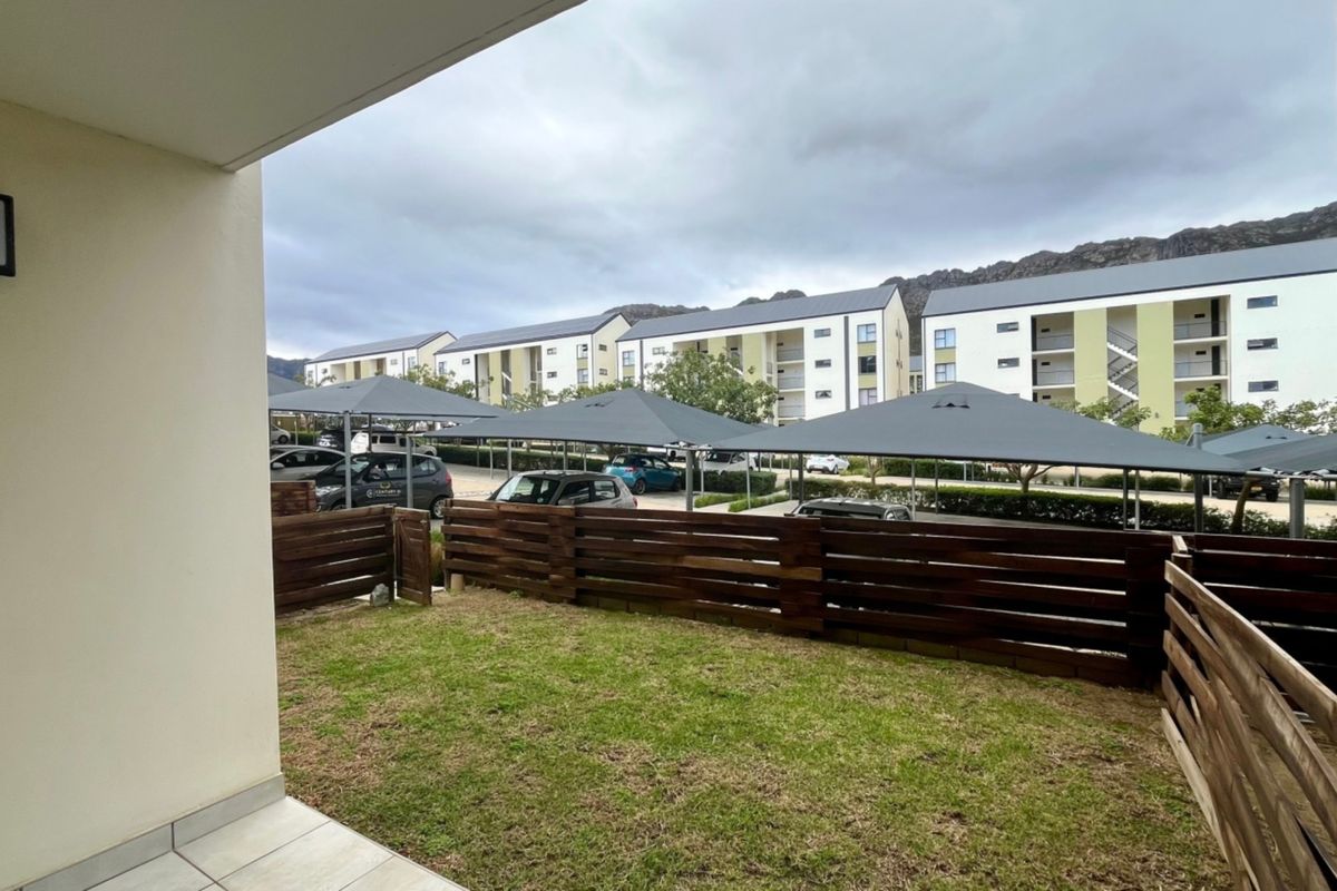 A private ground floor patio area featuring tiled flooring and timber slat fencing, overlooking the complex parking area with shade-net carports.
