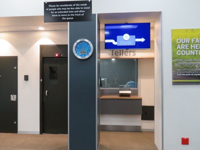 A clean, professional bank interior featuring a teller service area, secure access doors, and integrated digital signage for customer information.