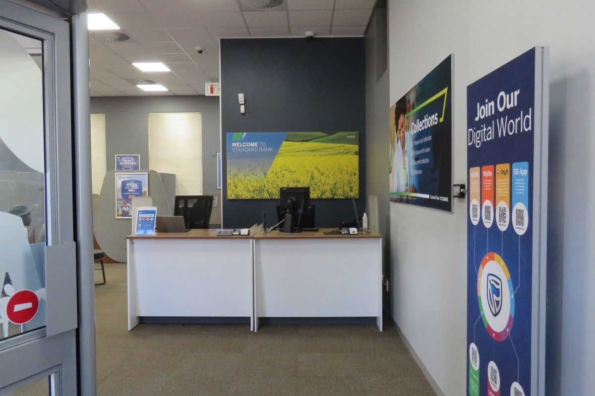 A professional bank branch entrance featuring a built-in reception desk, recessed lighting, and carpeted flooring in a clean, functional commercial space.