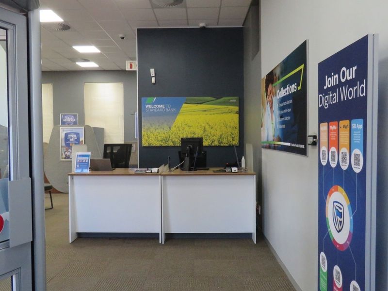 A professional bank branch entrance featuring a built-in reception desk, recessed lighting, and carpeted flooring in a clean, functional commercial space.