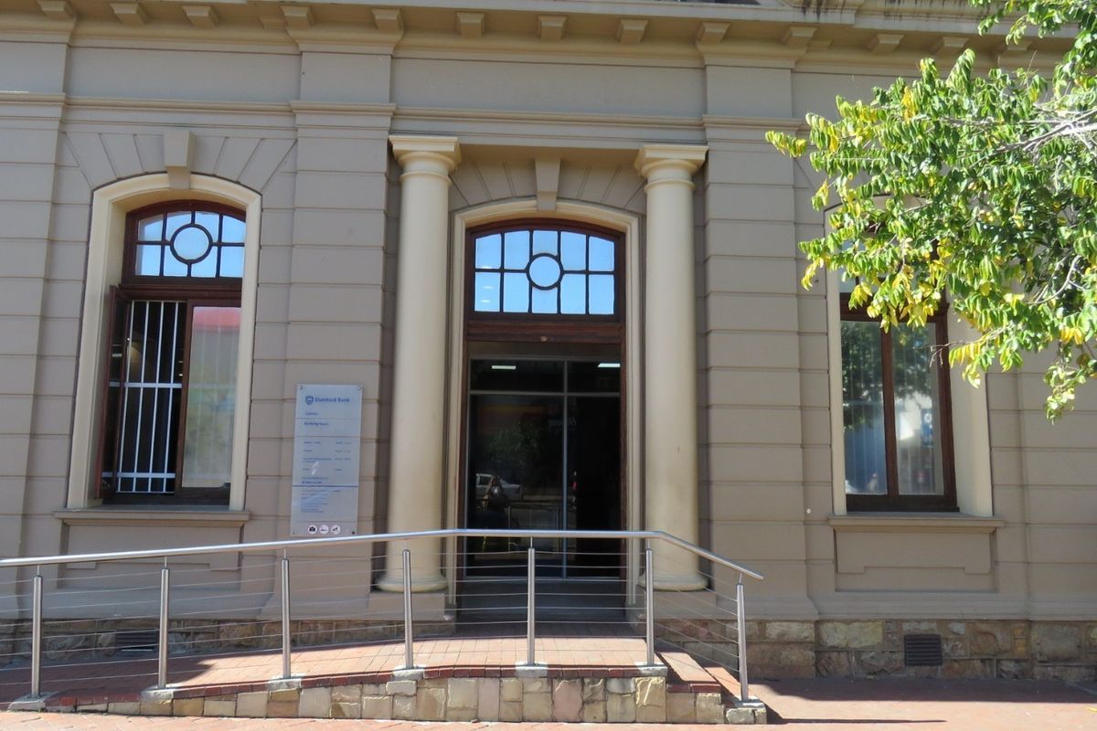 Front facade of a commercial building featuring classical architectural details, arched windows, and an accessible entrance ramp with stainless steel handrails.