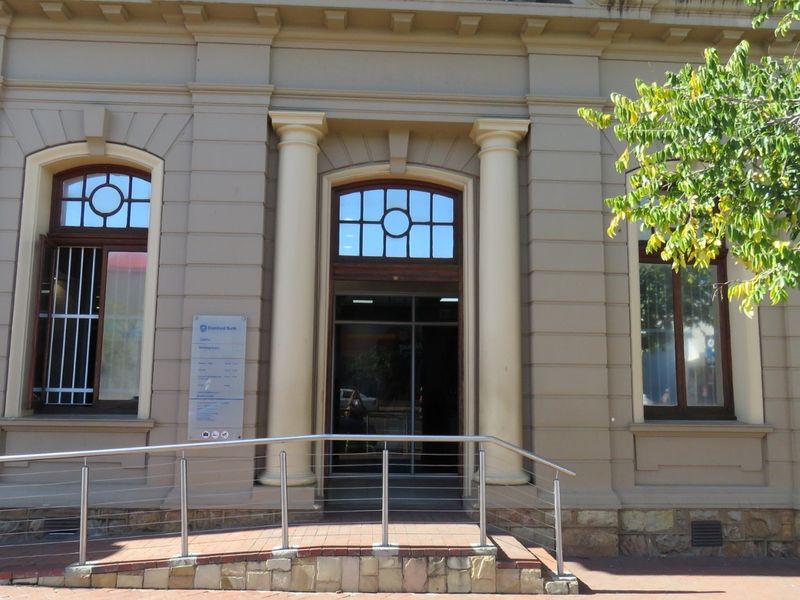 Front facade of a commercial building featuring classical architectural details, arched windows, and an accessible entrance ramp with stainless steel handrails.