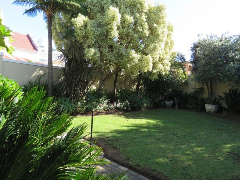 A well-maintained private garden featuring a lush lawn, mature trees, and a secure perimeter wall with a paved walkway.