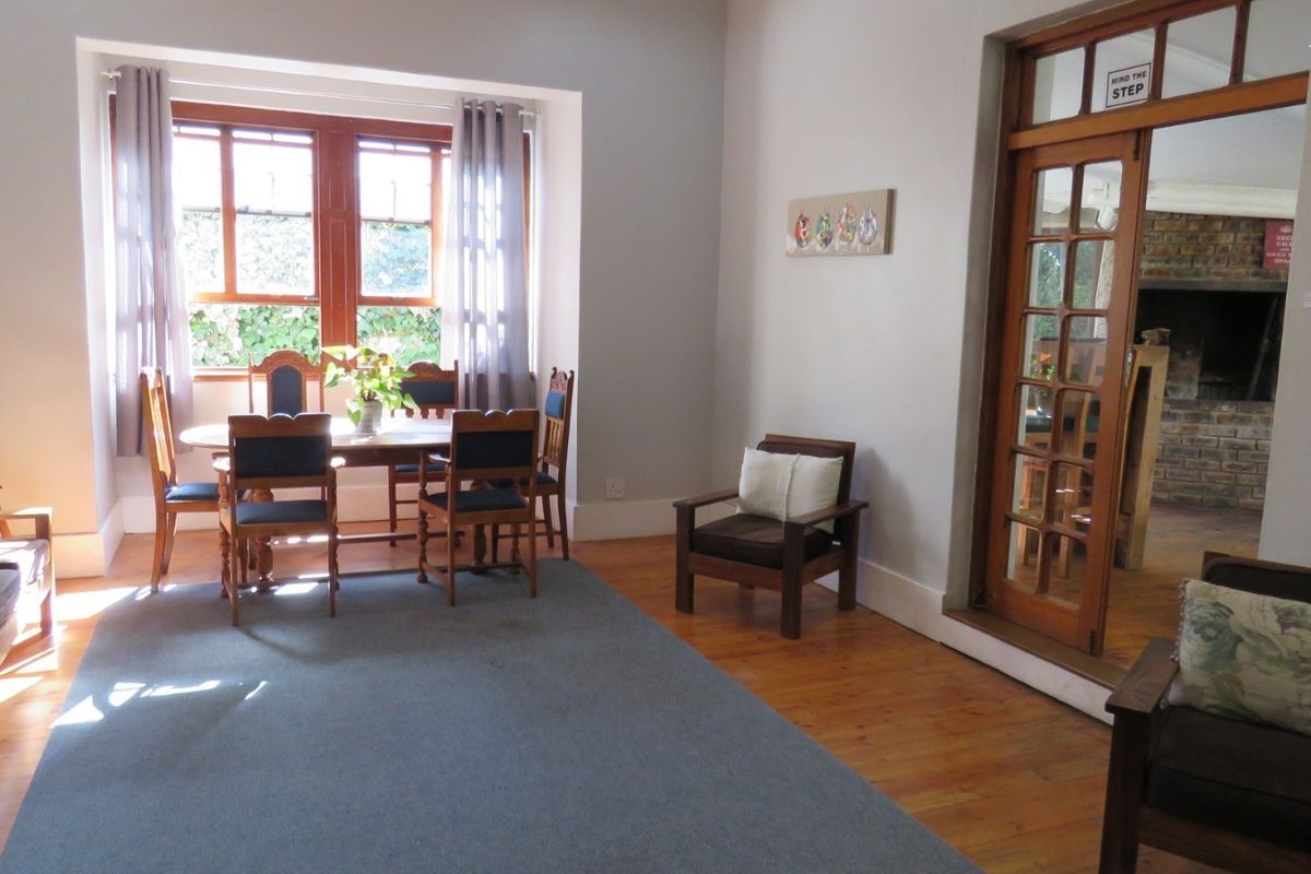 A spacious living area featuring polished timber flooring, large wooden-framed windows, and classic french doors leading to an adjacent room.