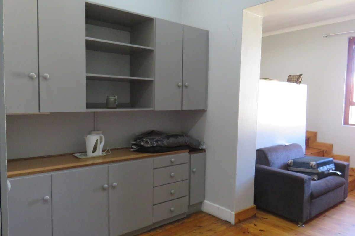 A functional kitchen area featuring grey built-in cabinetry, wooden countertops, and timber flooring, with an adjacent living space visible through the doorway.