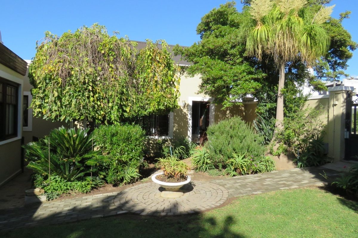 A well-maintained rear garden area featuring a paved circular walkway, established landscaping, and a secure wrought iron gate.